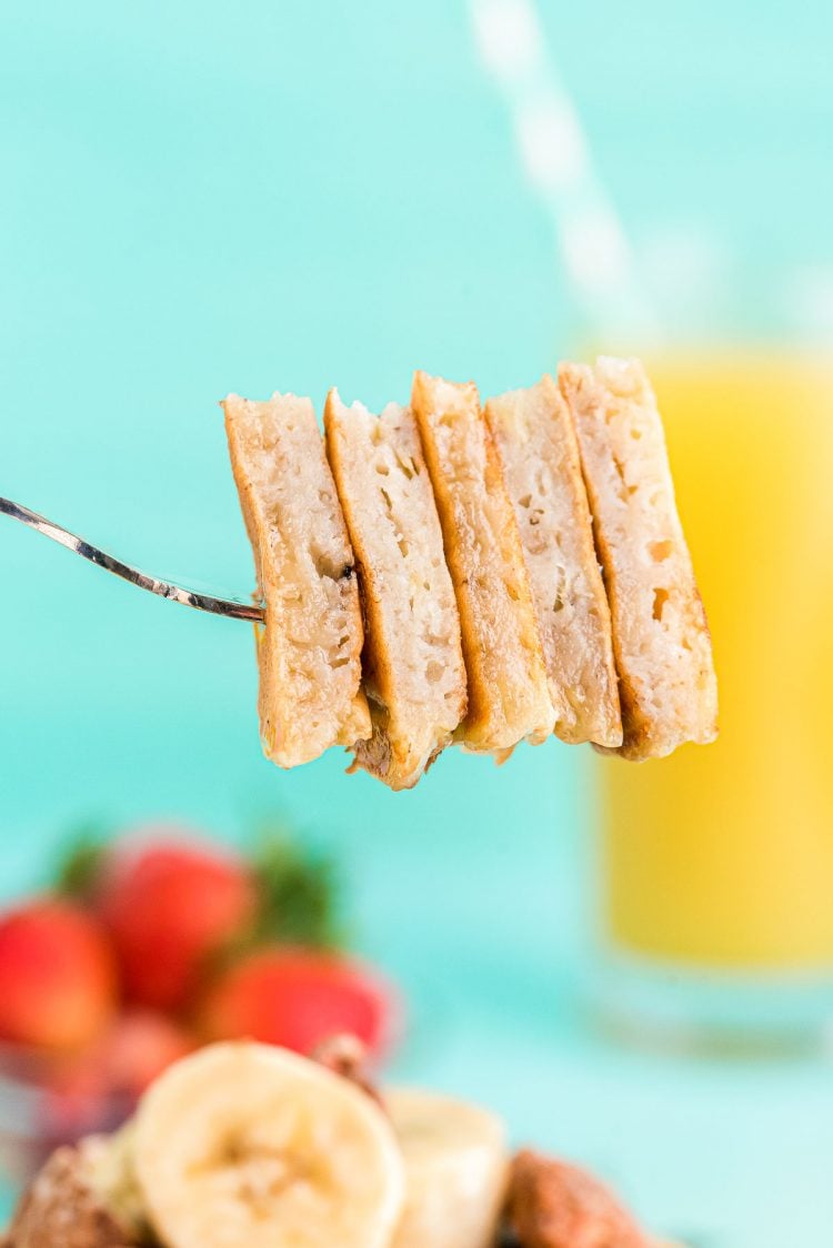 A fork with a bite size stack of banana pancake on it.