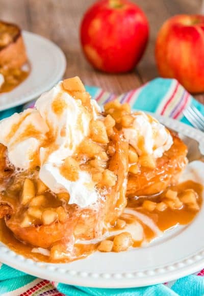 Apple french toast on a white plate topped with caramel and whipped cream.