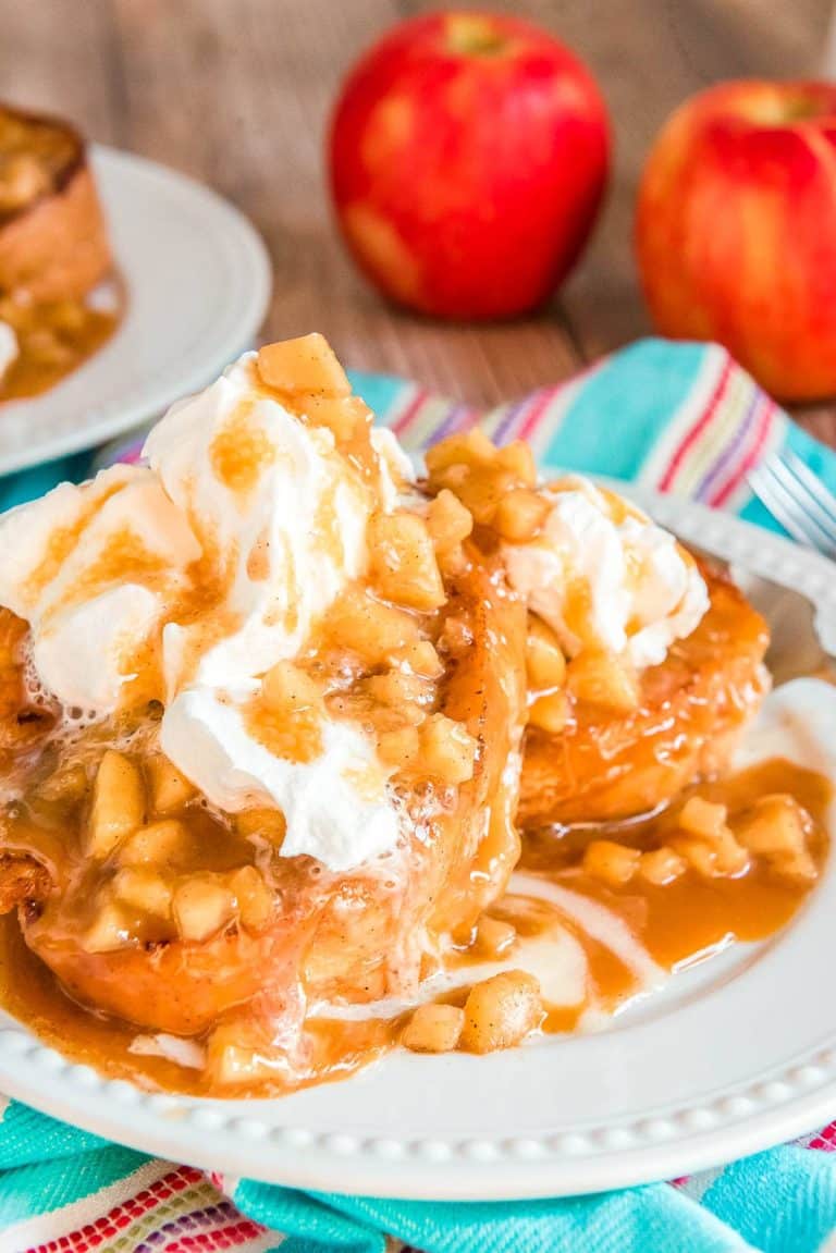 Apple french toast on a white plate topped with caramel and whipped cream.