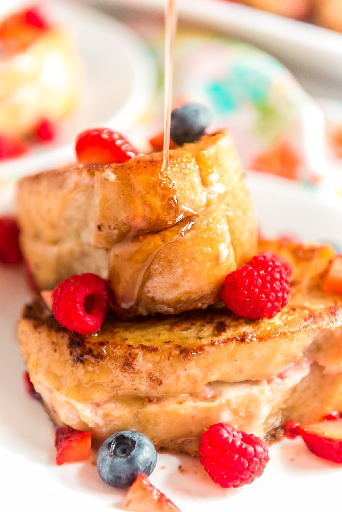 Maple Syrup being poured on a plate of french toast with berries.