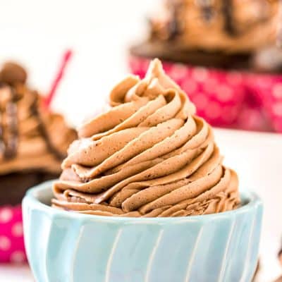 Chocolate Malt Frosting in a small blue bowl with cupcakes in the background.
