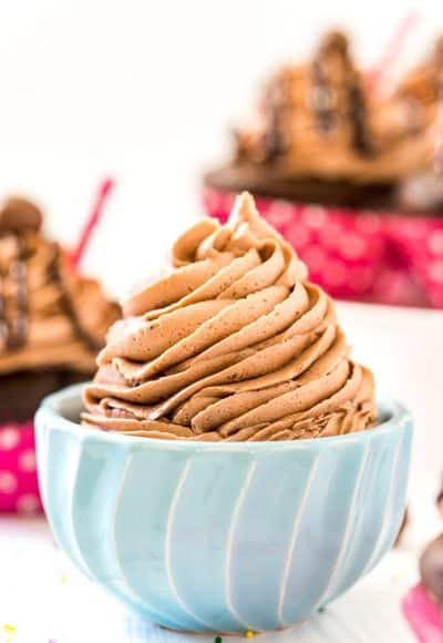 Chocolate Malt Frosting in a small blue bowl with cupcakes in the background.