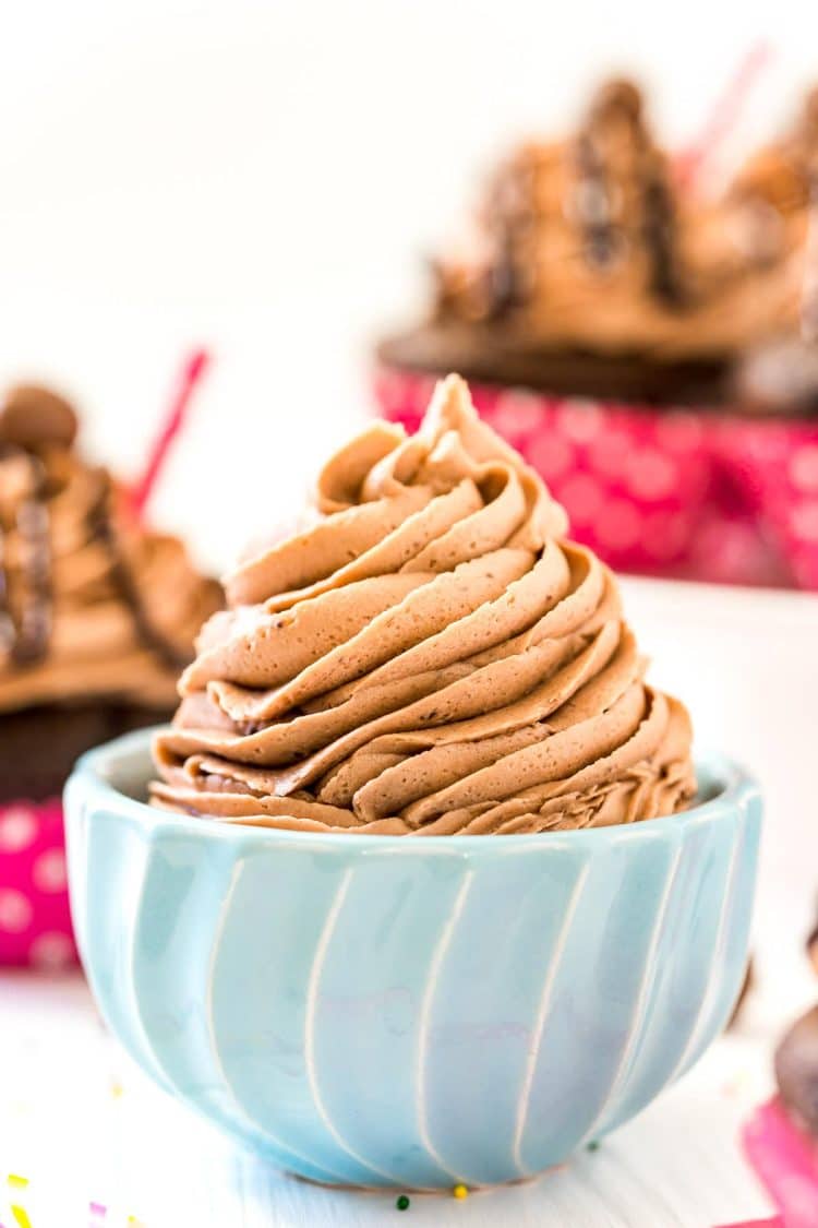 Chocolate Malt Frosting in a small blue bowl with cupcakes in the background.