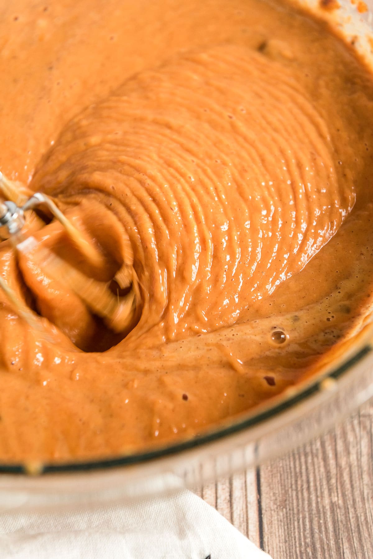 Pumpkin cake batter being mixed with a hand mixer in a large mixing bowl.