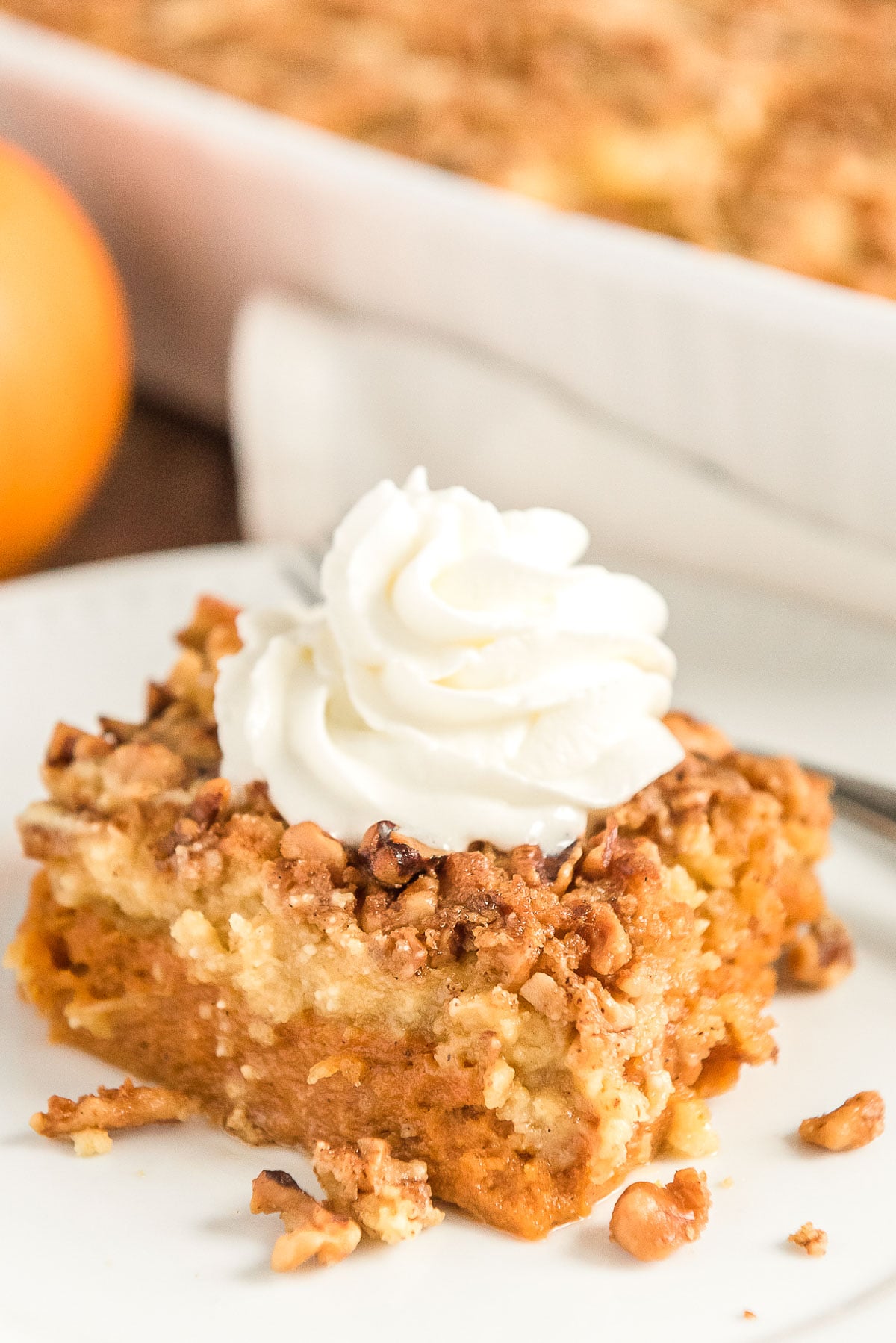 Close up photo of a slice of pumpkin dump cake on a white plate with pumpkin and more cake in background.