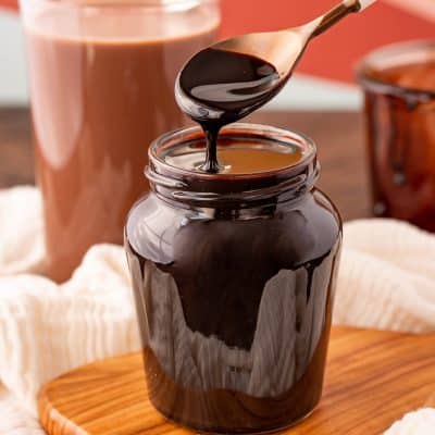 Chocolate syrup in a jar with a white spoon.