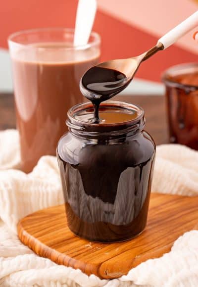 Chocolate syrup in a jar with a white spoon.