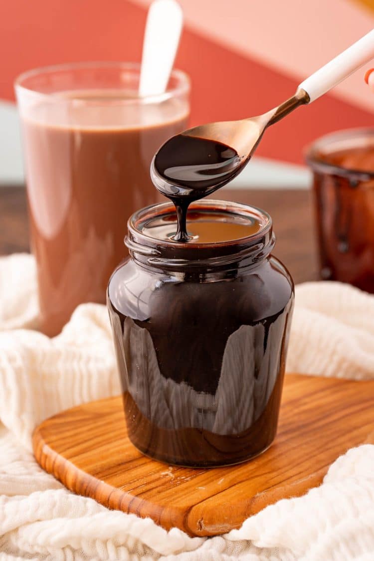 Chocolate syrup in a jar with a white spoon.