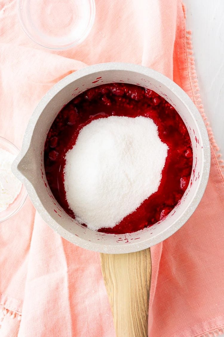 Sugar being added to a saucepan of raspberries.