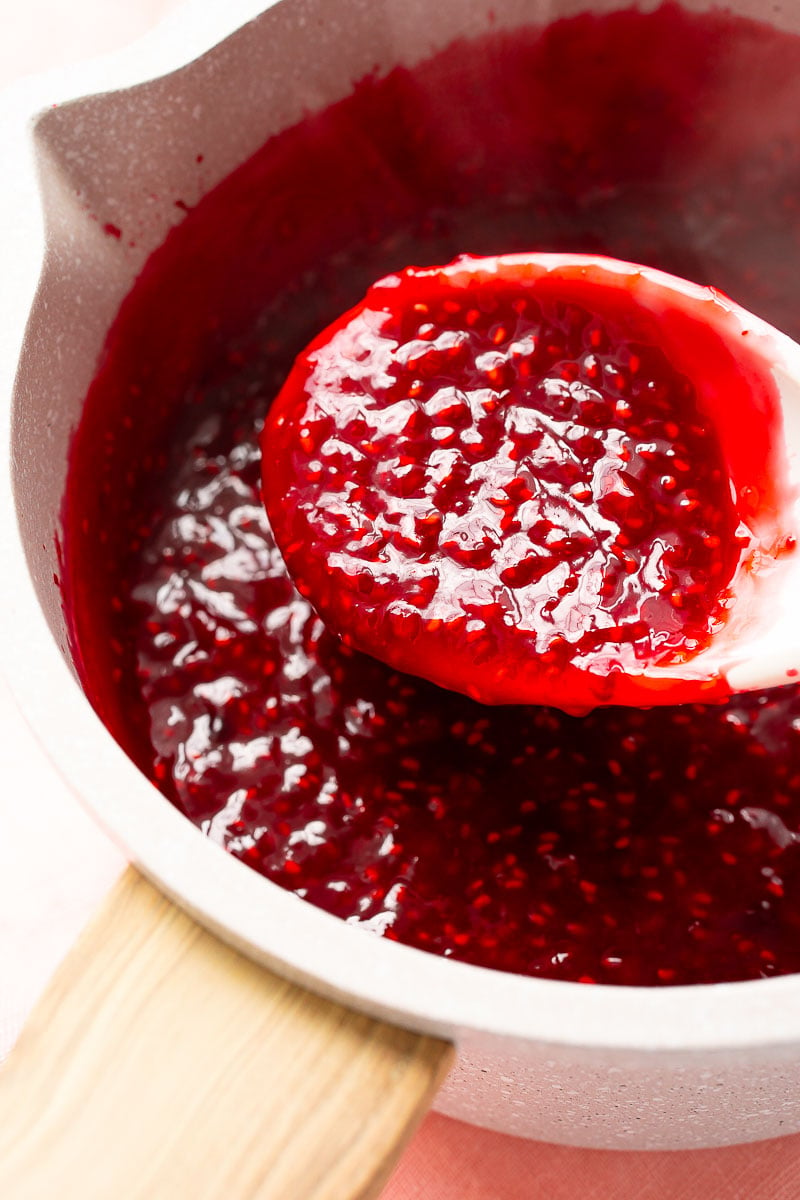 Raspberry filling in a saucepan with a white serving spoon scooping some of it out.