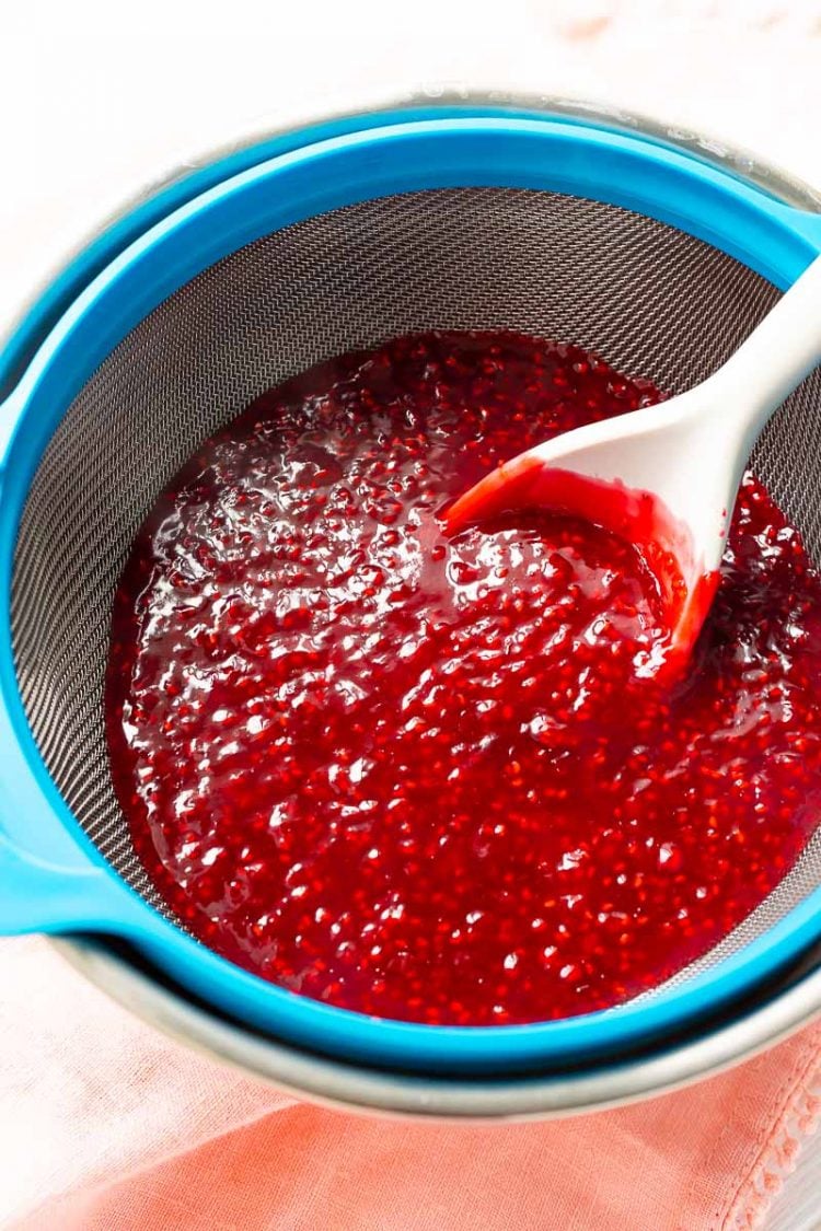 Raspberry sauce being run through a fine mesh strainer to remove seeds.