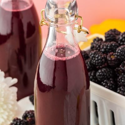 Close up of a bottle of blackberry simple syrup, another bottle and some berries in the background.