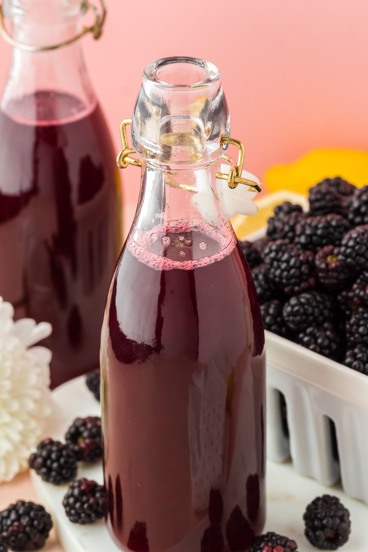 Close up of a bottle of blackberry simple syrup, another bottle and some berries in the background.