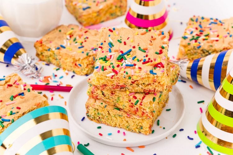 Close up photo of cake mix brownies on a white plate on a white table surrounded by sprinkles and birthday hats.