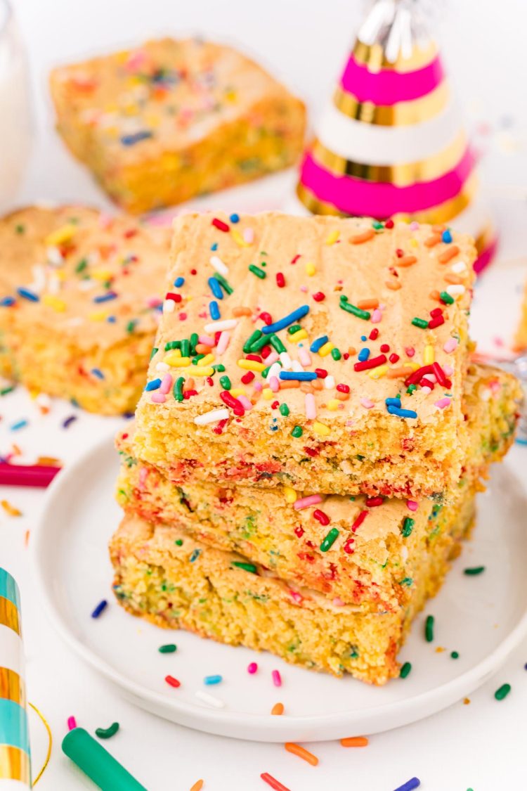 Close up photo of cake mix brownies on a white plate on a white table surrounded by sprinkles and birthday hats.