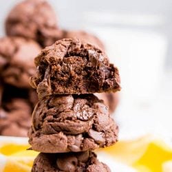 Three double chocolate chip cookies stacked on top of each other on a yellow napkin.