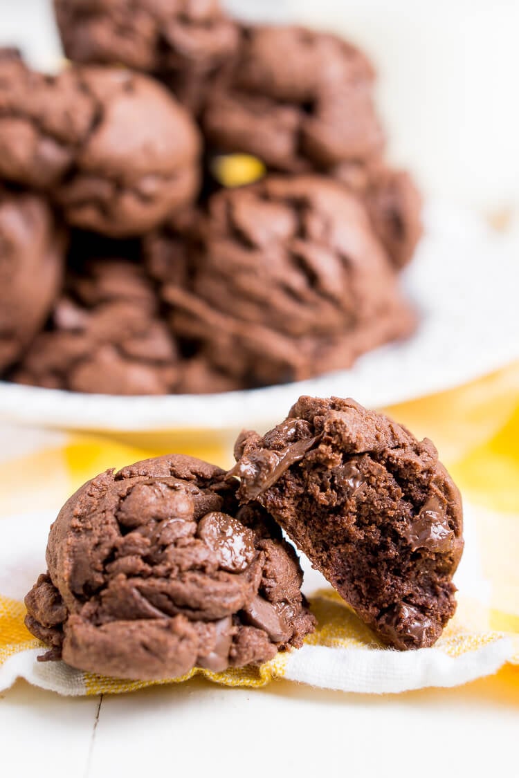 Two chocolate cookies on a yellow napkin in front of a plate with more cookies.