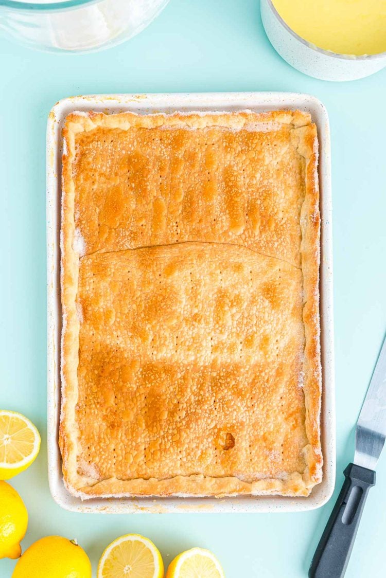 Pie crust that has been baked in a jelly roll pan on a blue surface with lemons around it.