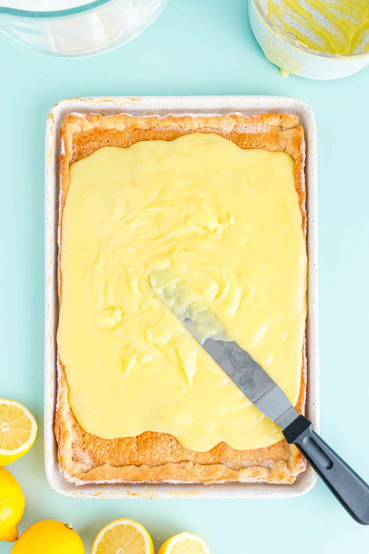 Lemon pie filling being spread over a baked pie crust on a jelly roll pan.