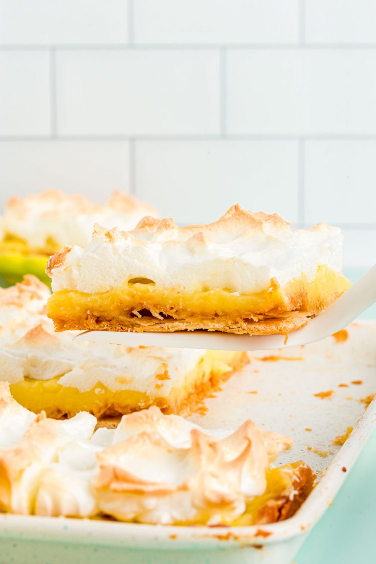 A slice of lemon meringue slab pie being lifted from the pan.