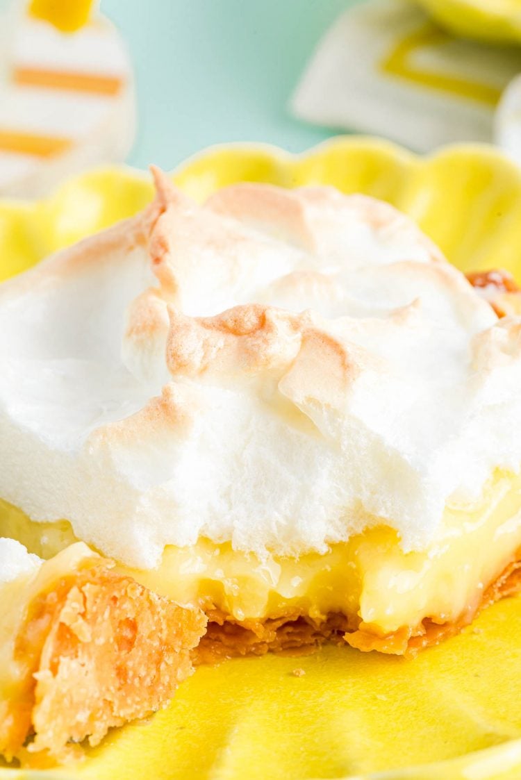 Close up photo of a slice of lemon meringue slab pie on a yellow plate with a bite taken out of it.