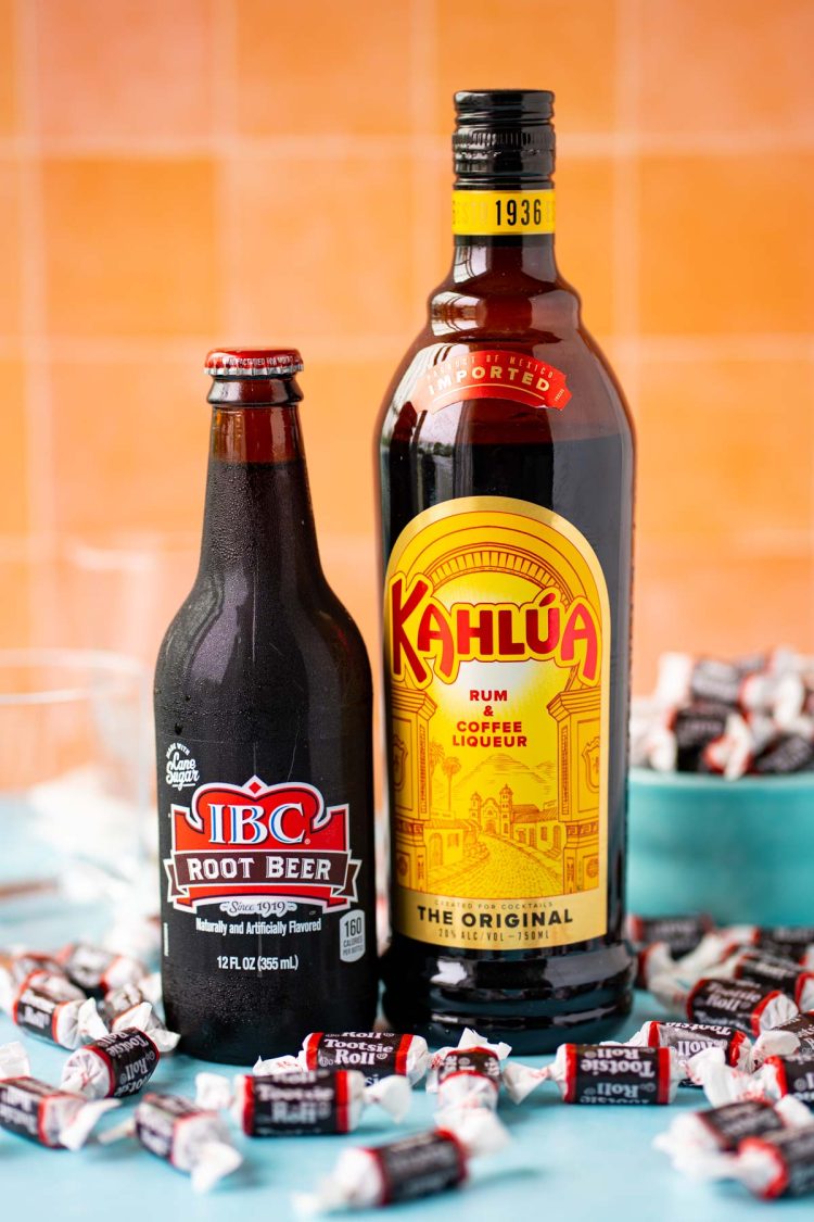 A bottle of root beer and kahlua on a blue table surrounded by tootsie rolls.