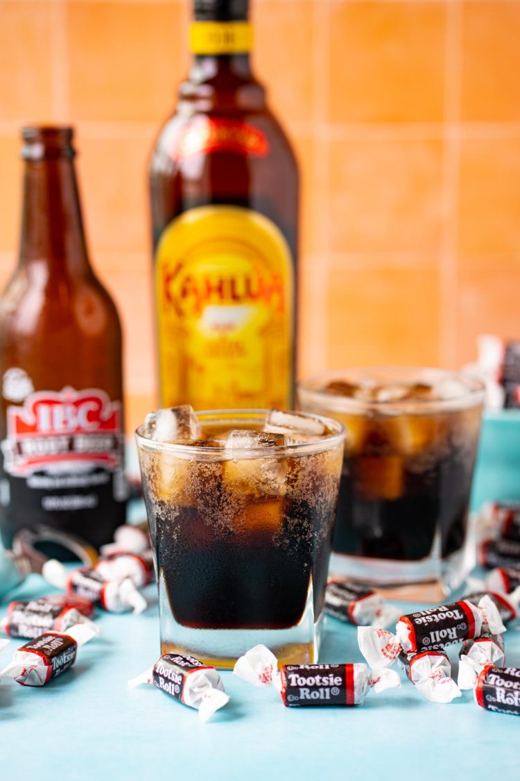 Two glasses with cocktail in them with a bottle of root beer and kahlua in the background.