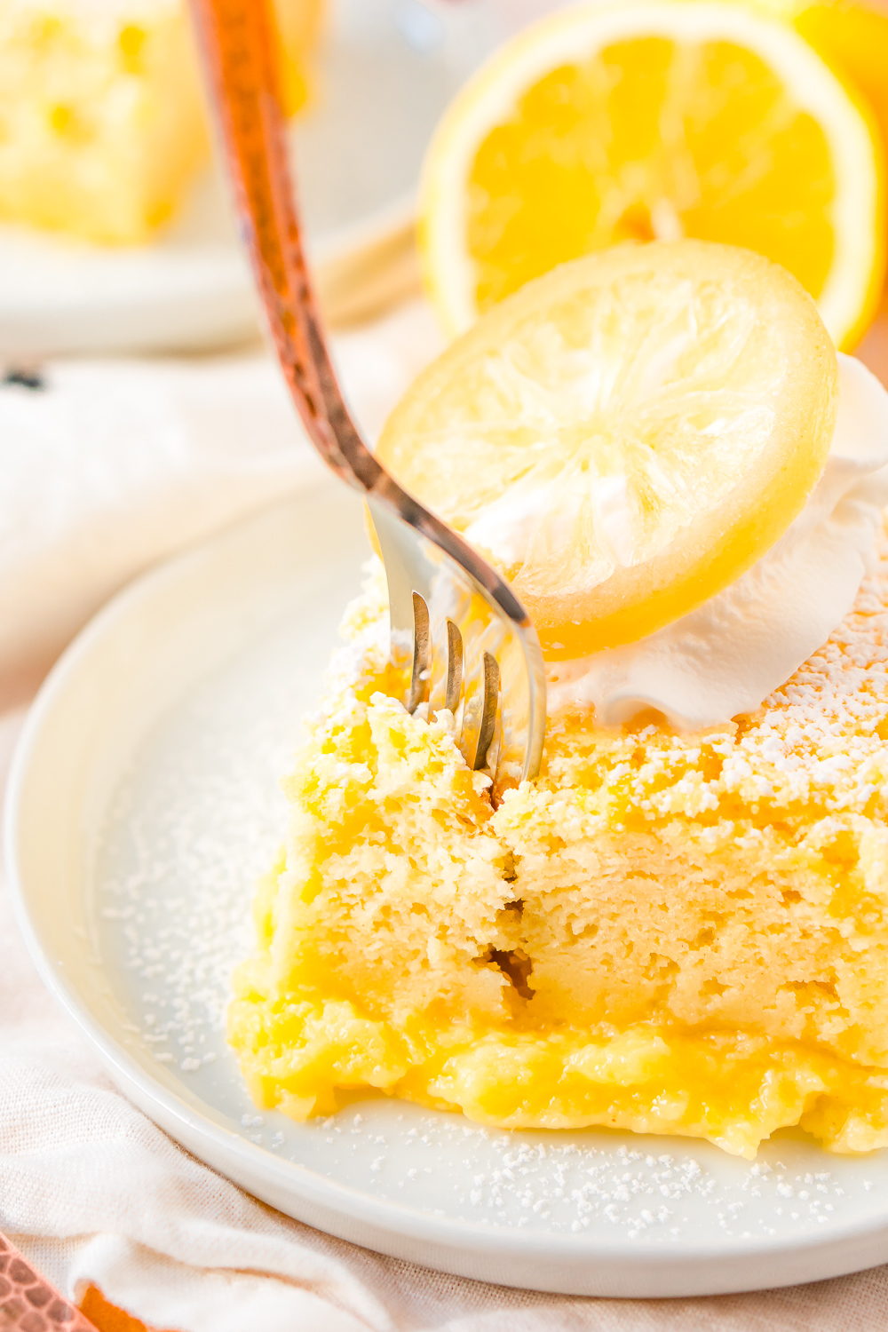 Fork digging into a slice of lemon cake on a small white plate.