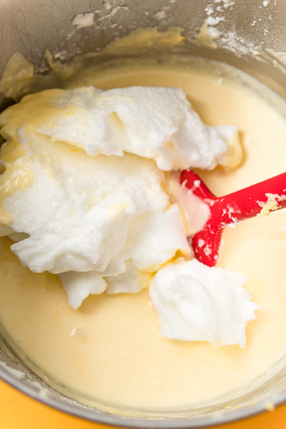 Stiff egg whites being folded into lemon cake batter in a metal mixing bowl.