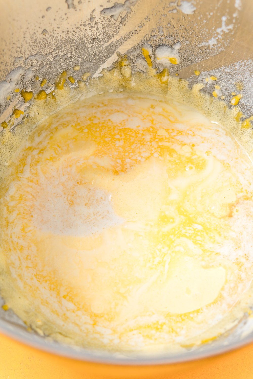Melted butter being added to lemon cake batter in metal mixing bowl.