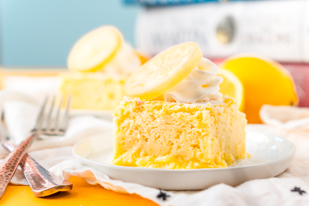 Horizontal photo of a piece of Lemon Magic Cake on a white plate with forks next to it.