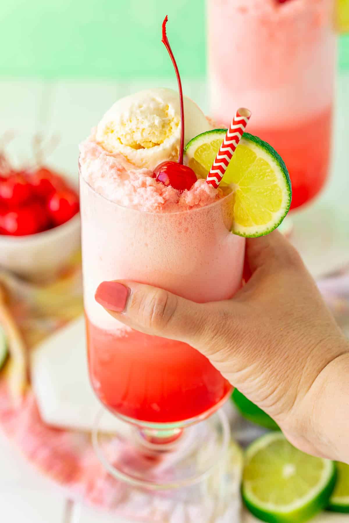 A woman's hand holding a glass filled with a shirley temple float to the camera.