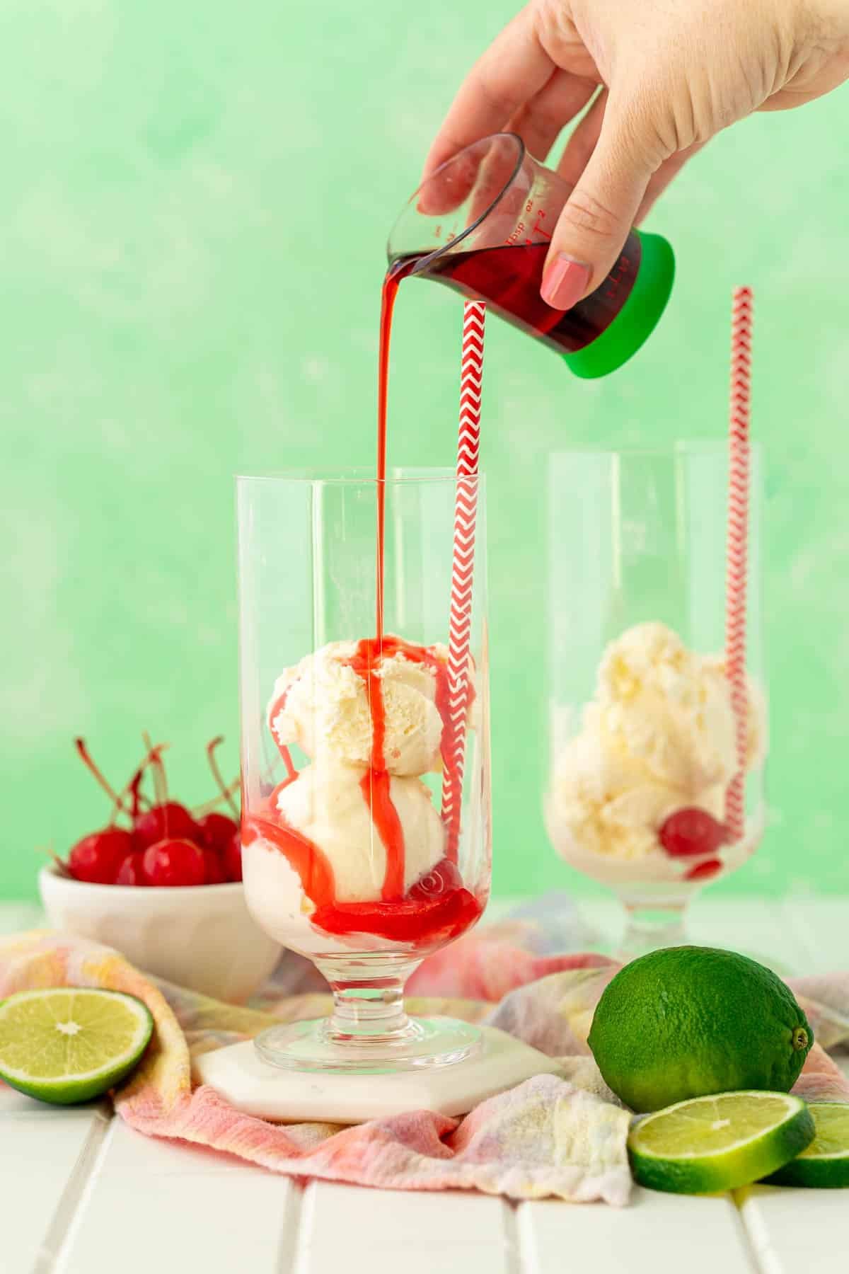 Grenadine syrup being poured over scoops of vanilla ice cream in a glass.