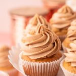 Close up photo of a french vanilla cupcake on a white cake stand with other cupcakes.