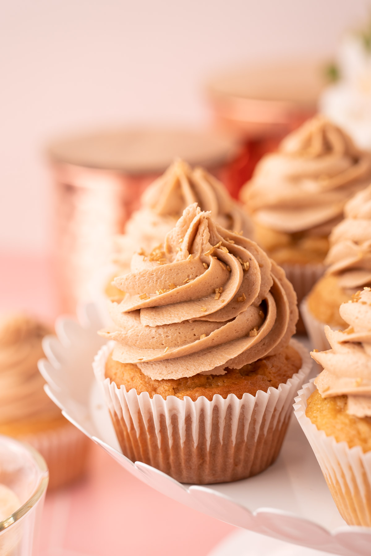 Close up photo of a french vanilla cupcake on a white cake stand with other cupcakes.