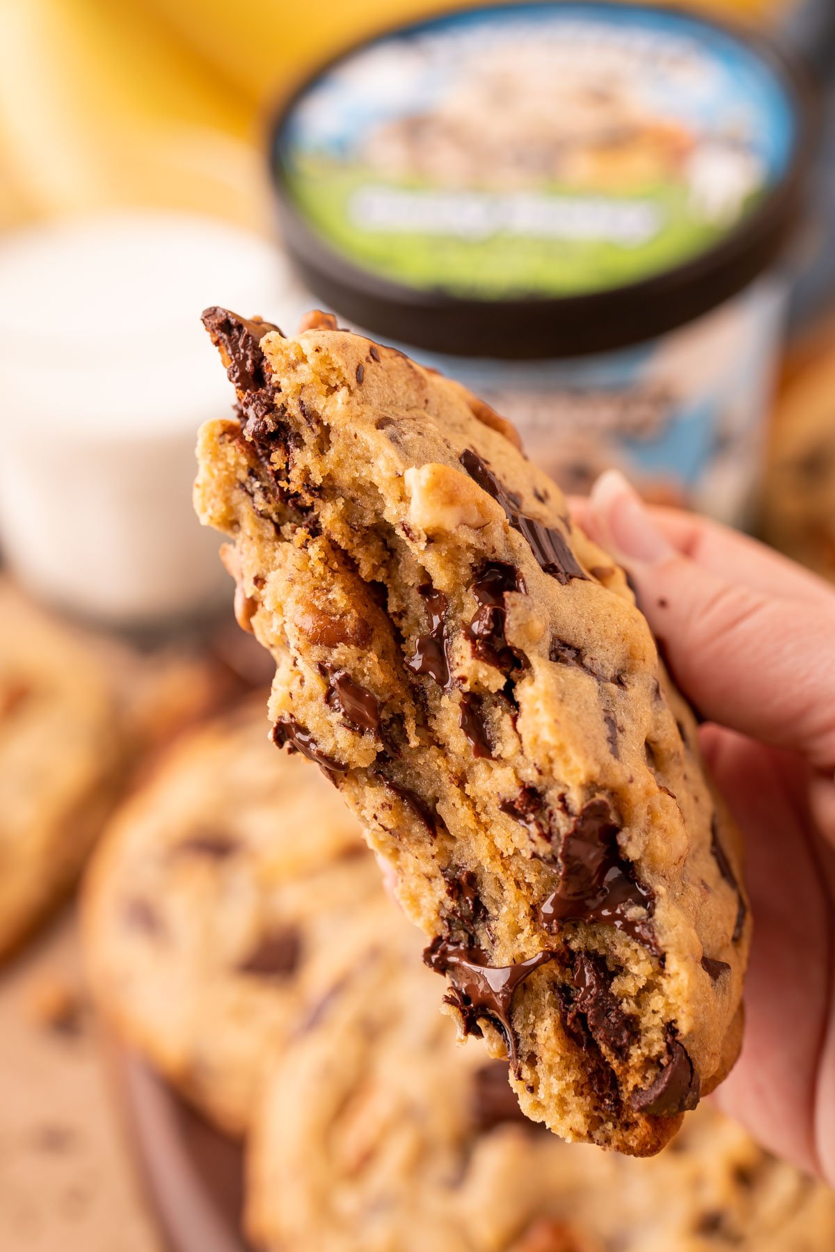 A woman's hand holding a broken in half chunky monkey cookies to show the inside texture.