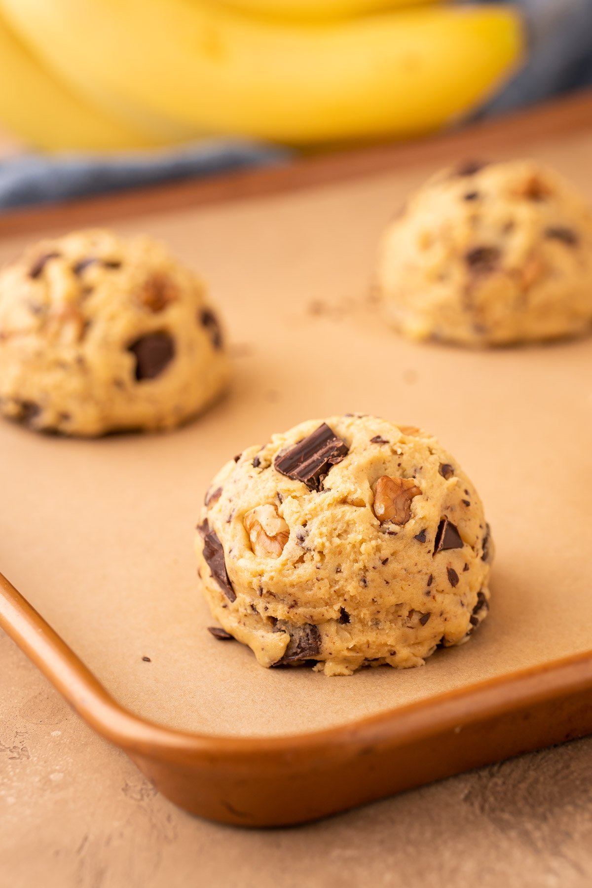 Scoops of chunky monkey cookie dough on a parchment lined baking sheet.