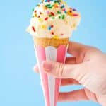Woman's hand holding a cone of vanilla ice cream with sprinkles on it.