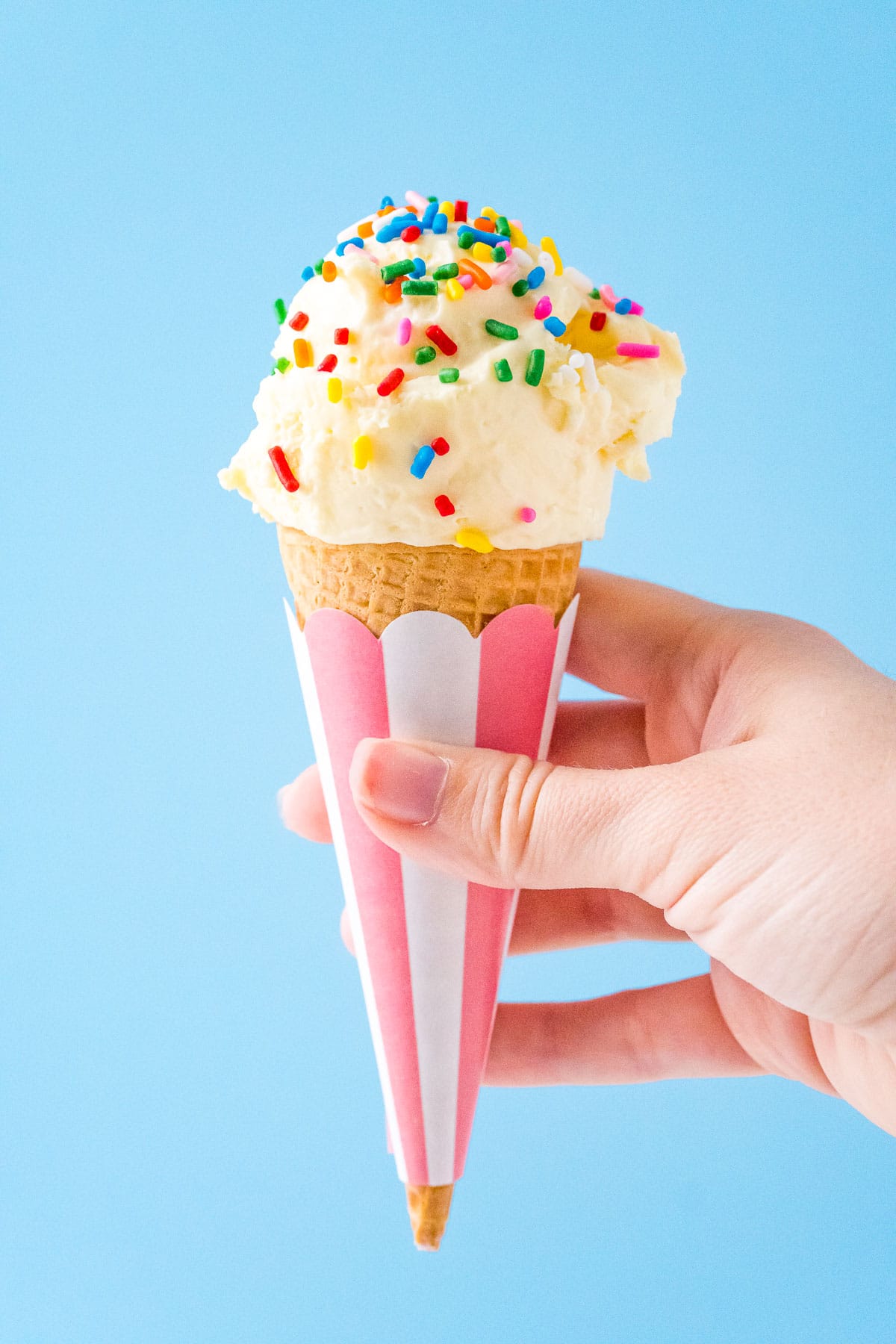 Woman's hand holding a cone of vanilla ice cream with sprinkles on it.