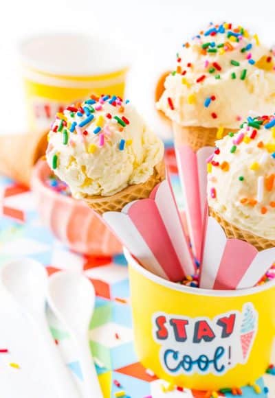 Three sugar cones with vanilla ice cream and sprinkles resting in a yellow bowl.
