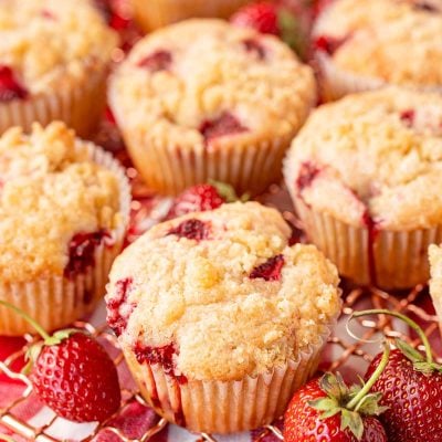 Strawberry muffins on a copper wire rack on a gingham napkin.