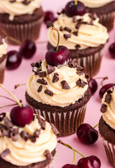 Black Forest Cupcakes on a pink surface surrounded by cherries.