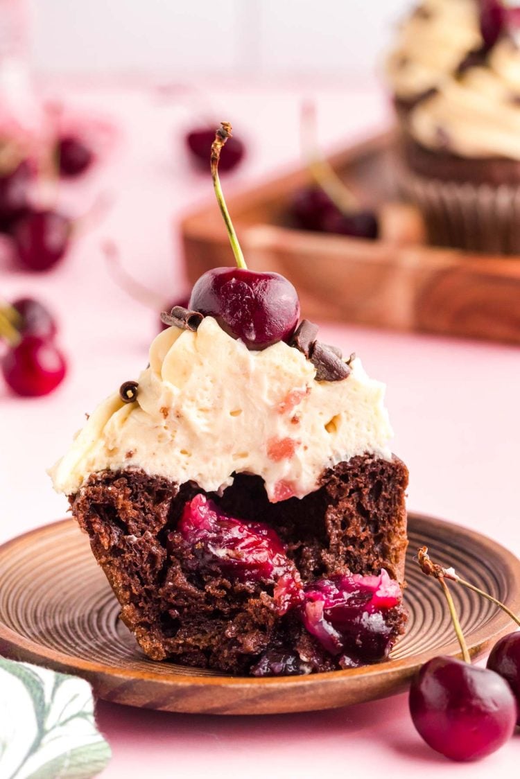 A black forest cupcake that's been cut in half to show the cherry filling on a wood plate.