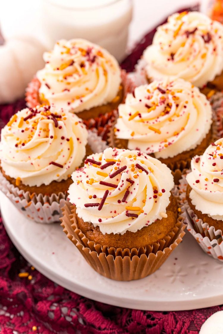 Pumpkin cupcakes on a white cake stand with a maroon napkin under it.