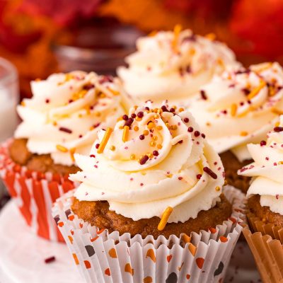 Close up photo of pumpkin cupcakes on a white cake stand with leaves in the background.
