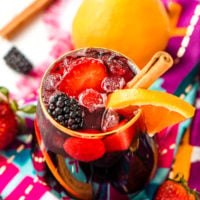 Glass filled with red sangria garnished with a cinnamon stick and and orange slice.