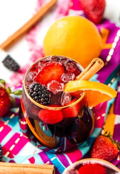 Glass filled with red sangria garnished with a cinnamon stick and and orange slice.