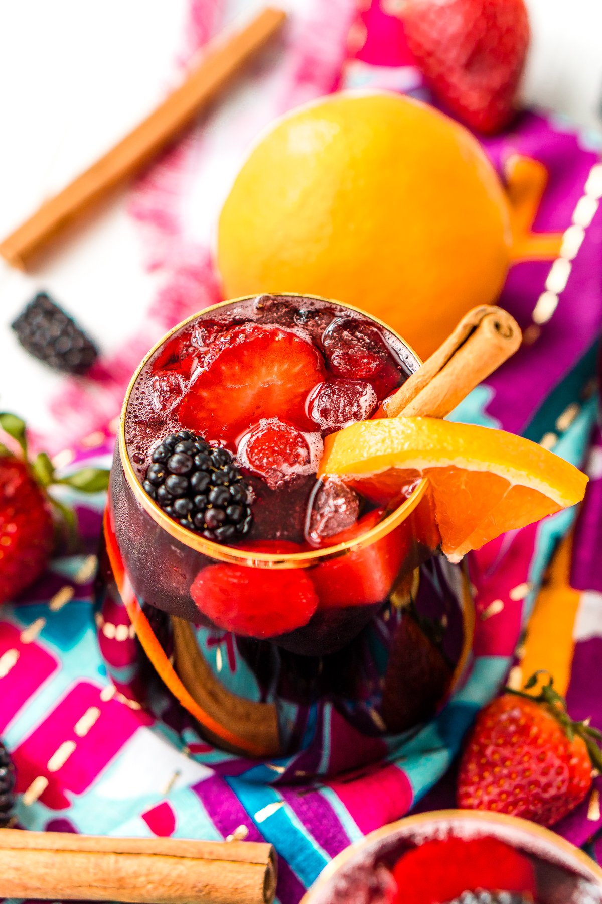 Glass filled with red sangria garnished with a cinnamon stick and and orange slice.