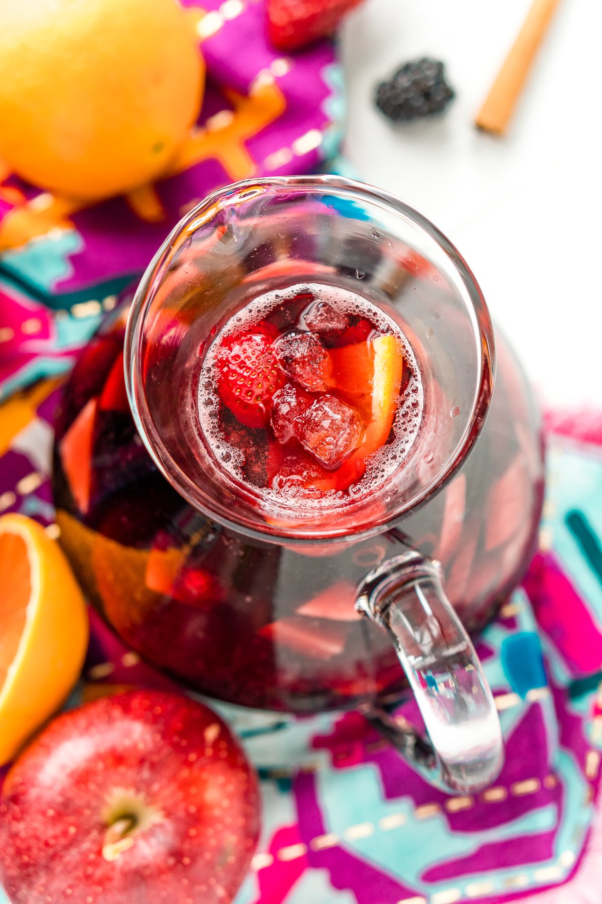 Overhead photo of a pitcher filled with red sangria made with apples, blackberries, oranges, and strawberries.