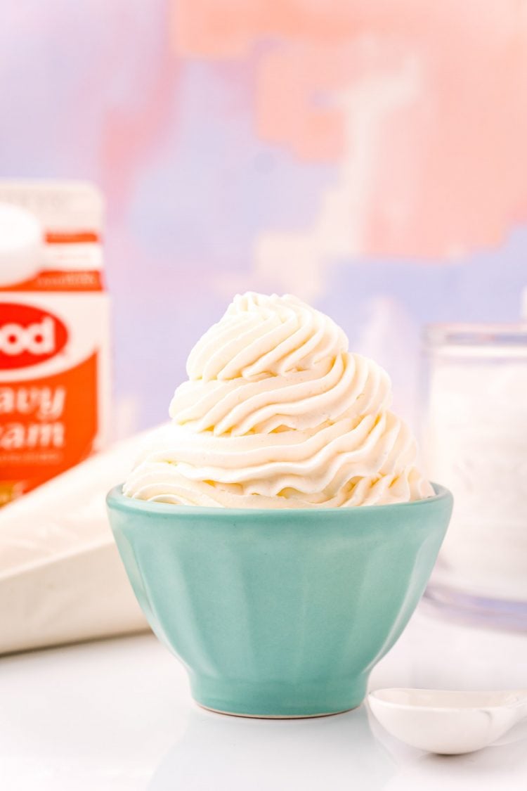 A small light blue bowl filled with piped whipped cream with a bag of whipped cream and a carton of heavy cream in the background.